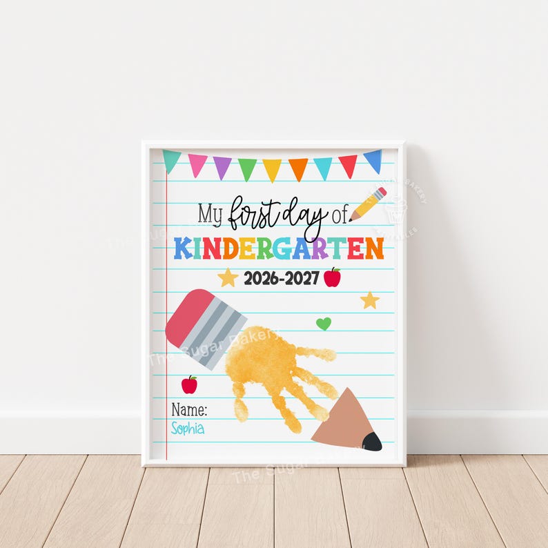 May include: A white poster with blue horizontal lines featuring the text My first day of KINDERGARTEN 2026-2027. It includes a colorful bunting, a yellow pencil, red apples, yellow stars, a green heart, and a yellow handprint shaped like a pencil.