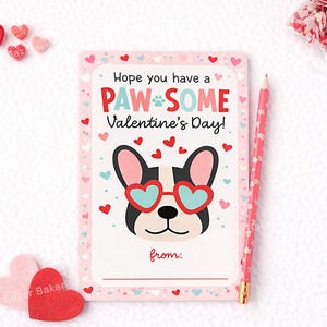 Puede incluir: Una tarjeta de San Valentín con borde rosa y un perro de dibujos animados con gafas de sol en forma de corazón. La tarjeta dice "Hope you have a PAW-SOME Valentine's Day!" con un espacio para escribir "from:". Un lápiz rosa y decoraciones en forma de corazón también están presentes.