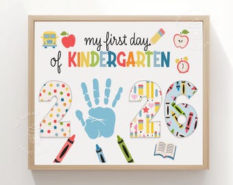 May include: A framed sign with the text my first day KINDERGARTEN 2026. The design features a light blue handprint in the center, a yellow school bus, red apple, pencil, and alarm clock. The numbers are decorated with colorful patterns.