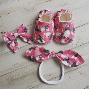 May include: Pink and white baby booties with a black and white motocross print. A matching pink and white headband with a bow is also included.