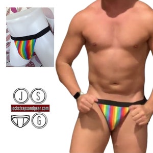 May include: Rainbow striped jockstrap with black waistband. The jockstrap is on a mannequin and a person wearing the jockstrap. The website "jockstrapsandgear.com" is visible in the image.