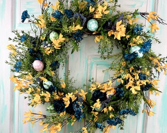 This unique yellow Chrysanthemums with blue flowers and easter eggs accent this large grapevine wreath with greenery for Easter door decor.