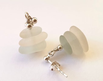 Puede incluir: Pendientes artesanales con vidrio marino y plata de ley. Cada pendiente presenta tres piezas ovaladas de vidrio marino esmerilado en blanco y verde pálido, apiladas y conectadas por un poste y alambre de plata. Diseño minimalista y de inspiración playera.