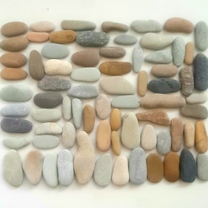 May include: A collection of smooth, flat stones in various shades of grey, brown, and beige. The stones are arranged in a rectangular pattern, creating a visually appealing mosaic.