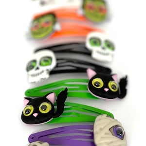 Pode incluir: Um conjunto de dez presilhas de cabelo com tema de Halloween. As presilhas apresentam v&aacute;rios designs, incluindo uma caveira, um gato, uma m&uacute;mia e um fantasma. As presilhas s&atilde;o feitas de pl&aacute;stico e t&ecirc;m um design colorido.