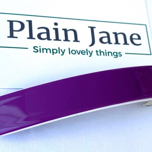 May include: A purple plastic hair clip with a white underside. The clip is curved and has a glossy finish.