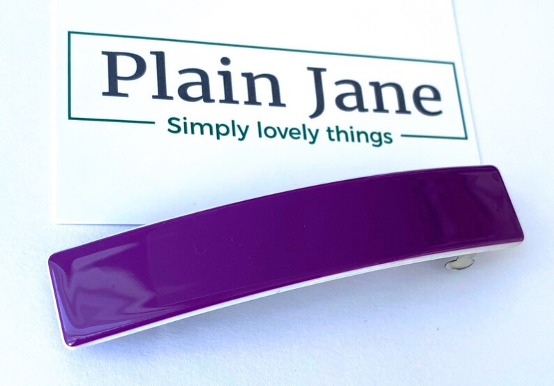 May include: A purple plastic hair clip with a white underside. The clip is curved and has a glossy finish.