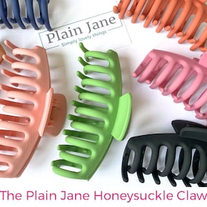 Puede incluir: Un conjunto de cuatro pinzas para el pelo en diferentes colores: rosa, verde, negro y naranja. Las pinzas tienen todas el mismo estilo, con una forma curva y varios dientes. El texto "Plain Jane - Simply lovely things" es visible en la imagen.