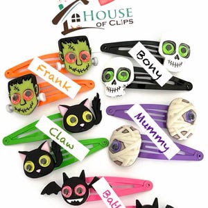 Pode incluir: Conjunto de dez presilhas de cabelo com tema de Halloween com olhos saltitantes. As presilhas representam personagens como uma m&uacute;mia, um esqueleto, um gato, um morcego e um monstro de Frankenstein. Cada presilha tem uma etiqueta com um nome, como "Frank", "Bony", "Claw", "Batty" e "Mummy".