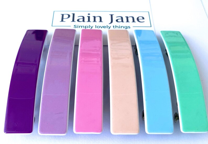 May include: Six colorful plastic hair clips in a rainbow color scheme. The clips are arranged in a row from left to right: purple, lavender, pink, peach, light blue, and mint green.