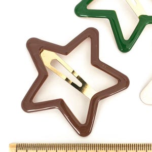 Pu&ograve; includere: Fermagli per capelli a forma di stella marroni e verdi con chiusure in metallo color oro. Gli accessori per capelli sono mostrati su sfondo bianco con un righello per la scala. I fermagli a forma di stella misurano circa 5 cm di lunghezza.