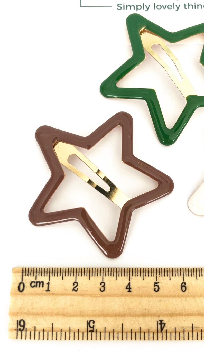 Pu&ograve; includere: Fermagli per capelli a forma di stella marroni e verdi con chiusure in metallo color oro. Gli accessori per capelli sono mostrati su sfondo bianco con un righello per la scala. I fermagli a forma di stella misurano circa 5 cm di lunghezza.