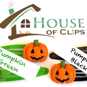 Op de afbeelding: Twee Halloween-haarclips met oranje pompoen-vormige bedels. De bedels hebben zwarte ogen, een neus en een glimlachende mond. De clips zijn gelabeld "Pumpkin Green" en "Pumpkin Black".