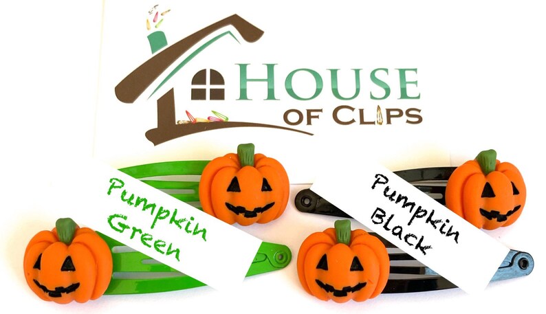 Op de afbeelding: Twee Halloween-haarclips met oranje pompoen-vormige bedels. De bedels hebben zwarte ogen, een neus en een glimlachende mond. De clips zijn gelabeld "Pumpkin Green" en "Pumpkin Black".
