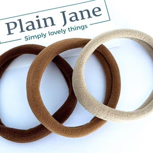 May include: Three hair scrunchies in brown, dark brown, and beige. The scrunchies are made of soft, stretchy fabric.