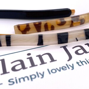 May include: Three hair clips, one black, one with a leopard print, and one with black and white stripes. The clips are on a white surface with the text "Plain Jane - simply lovely things" printed on it.