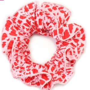 May include: A pink and red scrunchie with a leopard print pattern. The scrunchie is made of fabric and has a ruffled edge.