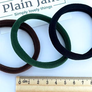 May include: Three hair ties in brown, green, and black. The hair ties are shown next to a ruler with measurements in centimeters.