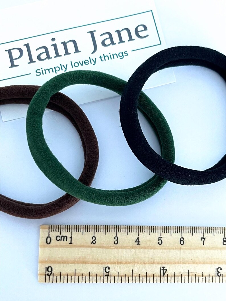 May include: Three hair ties in brown, green, and black. The hair ties are shown next to a ruler with measurements in centimeters.