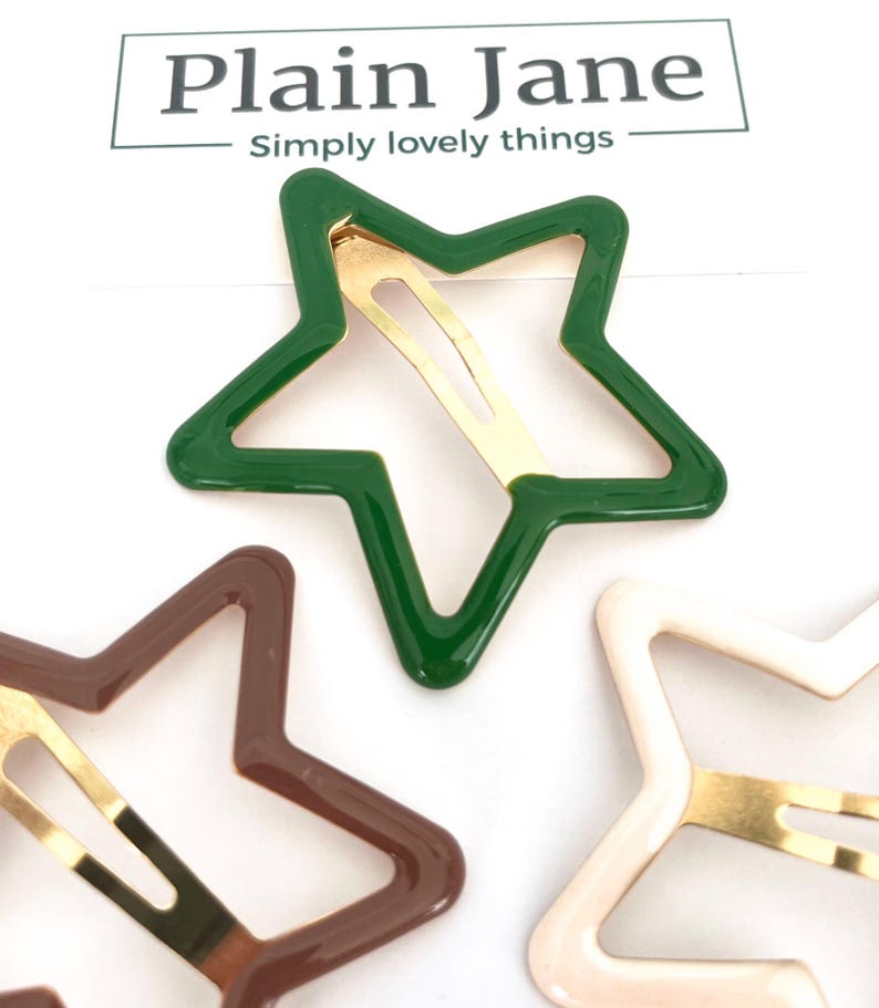 Pu&ograve; includere: Fermagli per capelli a forma di stella nei colori verde, marrone e crema. Ogni fermaglio ha una chiusura in metallo color oro. Il marchio "Plain Jane" &egrave; stampato nella parte superiore dell'immagine.