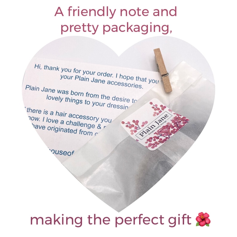 May include: A heart-shaped white paper bag with a handwritten note inside. The note says "Hi, thank you for your order. I hope that you your Plain Jane accessories. Plain Jane was born from the desire to lovely things to your dressin there is a hair accessory you now. I love a challenge & r have originated from  ouseof"  The bag is closed with a wooden clothespin. A small pink and white sticker with the text "Plain Jane Simply lovely things" is on the bag.