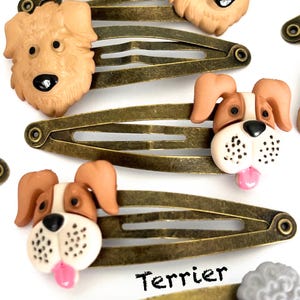 May include: Several bronze-toned metal hair clips with dog-shaped embellishments. The dog faces are tan, brown, and white, with black eyes and pink tongues. The word "Terrier" is printed in black.
