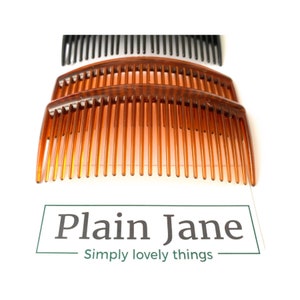 May include: Two brown plastic hair combs with a curved shape. The combs are stacked on top of each other. The text "Plain Jane Simply lovely things" is printed on a white background.