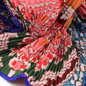 May include: Close-up of a pleated fabric with a colorful floral pattern. The fabric is pink, orange, green, blue, and white. The fabric has a blue trim.