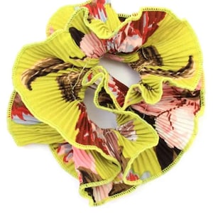 May include: A yellow, ruffled hair scrunchie with a floral print. The scrunchie has a green trim and a pink, red, and brown floral pattern.