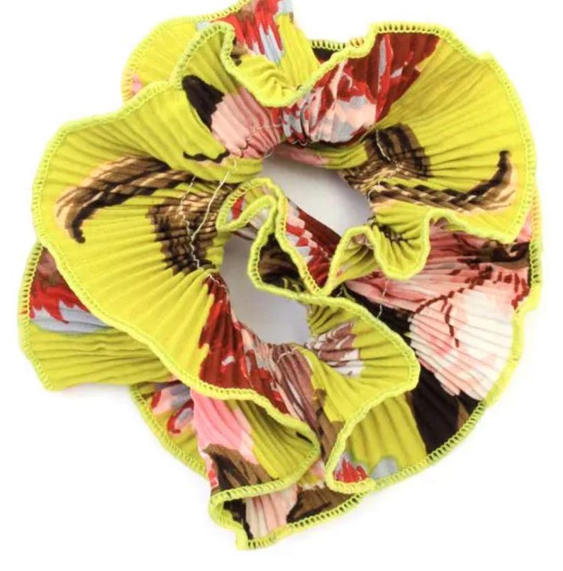 May include: A yellow, ruffled hair scrunchie with a floral print. The scrunchie has a green trim and a pink, red, and brown floral pattern.
