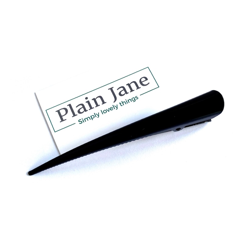 May include: A black hair clip with a pointed design. The clip is made of a shiny material and has a simple, elegant look. The text "Plain Jane Simply lovely things" is on a white card.