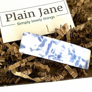 Op de afbeelding: Een rechthoekige staaf met een witte basis en blauwe bloempatronen rust op bruine papieren vulling. Een witte kaart met de tekst "Plain Jane" en "Simply lovely things" staat op de achtergrond.