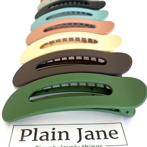 May include: A selection of colourful hair clips in shades like green, brown, and blue. The clips are arranged in a row, highlighting their curved design and matte finish. The text "Plain Jane" is visible at the bottom of the image.