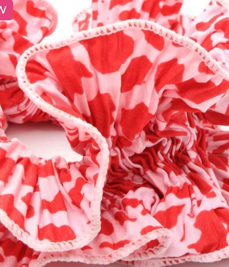 May include: Close-up of a red and pink patterned hair scrunchie. The scrunchie is made of fabric with a ruffled edge.