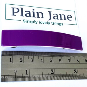 May include: A purple plastic hair clip measuring approximately 2 inches in length. The clip is curved and has a white underside.