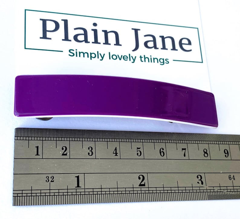 May include: A purple plastic hair clip measuring approximately 2 inches in length. The clip is curved and has a white underside.