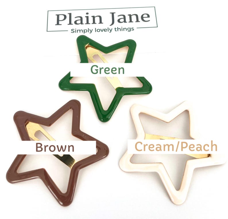 Pu&ograve; includere: Tre fermagli per capelli a forma di stella in verde, marrone e crema/pesca. Ogni fermaglio ha una base in metallo dorato. La parte superiore dell'immagine presenta il testo "Plain Jane" e "Simply lovely things".