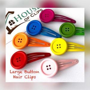 以下が含まれることがあります： ピンク、イエロー、レッド、ブルー、グリーン、オレンジなど、さまざまな色の大きなボタン付きヘアクリップ7個セット。各クリップには、4つの穴のある大きなボタンが付いています。クリップには「Large Button Hair Clips」というラベルが付いています。