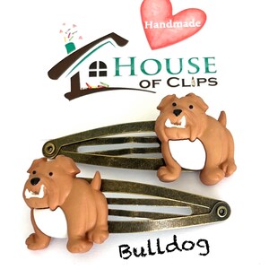 May include: Two bronze-toned metal hair clips, each adorned with a brown bulldog figurine with a white belly. The clips are set against a white background, with the word "Bulldog" and the "House of Clips" logo visible.