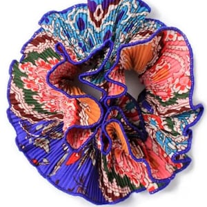 May include: A colorful hair scrunchie with a blue, orange, pink, and green paisley pattern. The scrunchie is made of pleated fabric and has a blue trim.