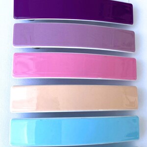 May include: Six colorful plastic hair clips in a rainbow color scheme. The clips are arranged in a stack from top to bottom: purple, lavender, pink, peach, light blue, and green.
