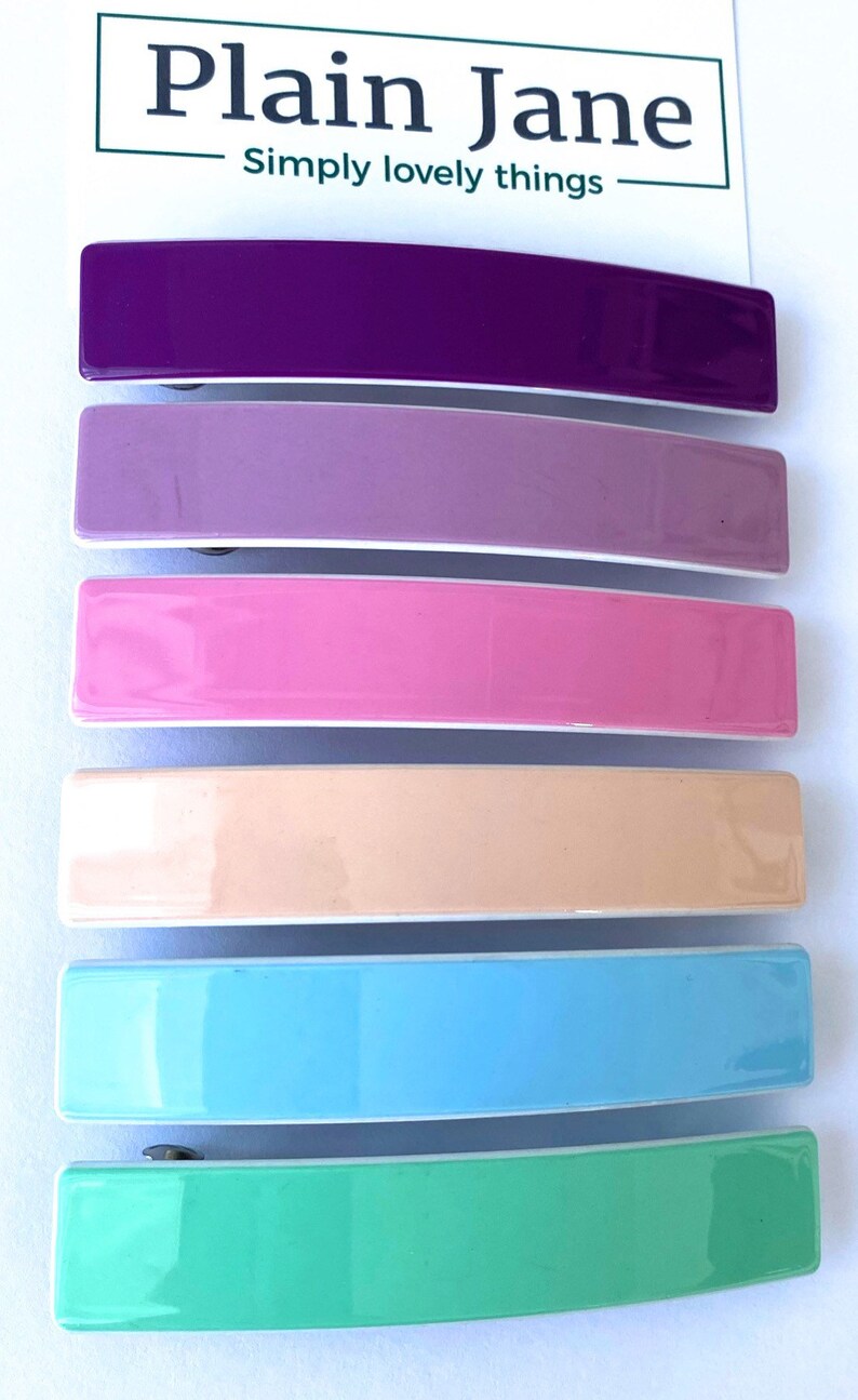 May include: Six colorful plastic hair clips in a rainbow color scheme. The clips are arranged in a stack from top to bottom: purple, lavender, pink, peach, light blue, and green.