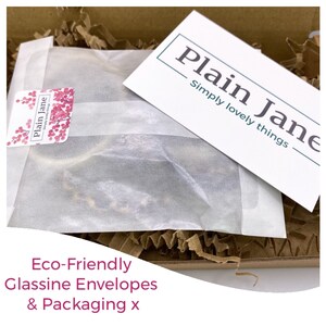 May include: A white paper envelope with a small sticker that says "Plain Jane Simply Lovely Things" on it. The envelope is sitting on brown packing peanuts inside a cardboard box. The text "Eco-Friendly Glassine Envelopes & Packaging x" is visible at the bottom of the image.