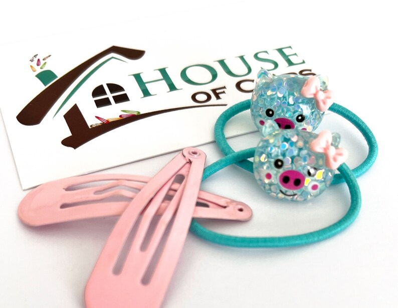 May include: Two turquoise hair ties with a blue pig face charm and a pink bow. Two pink hair clips.