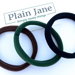 May include: Three hair scrunchies in brown, green, and black. The scrunchies are made of a soft, stretchy fabric.