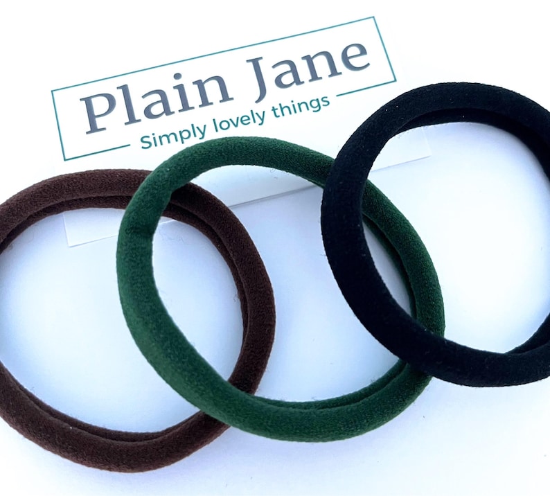 May include: Three hair scrunchies in brown, green, and black. The scrunchies are made of a soft, stretchy fabric.