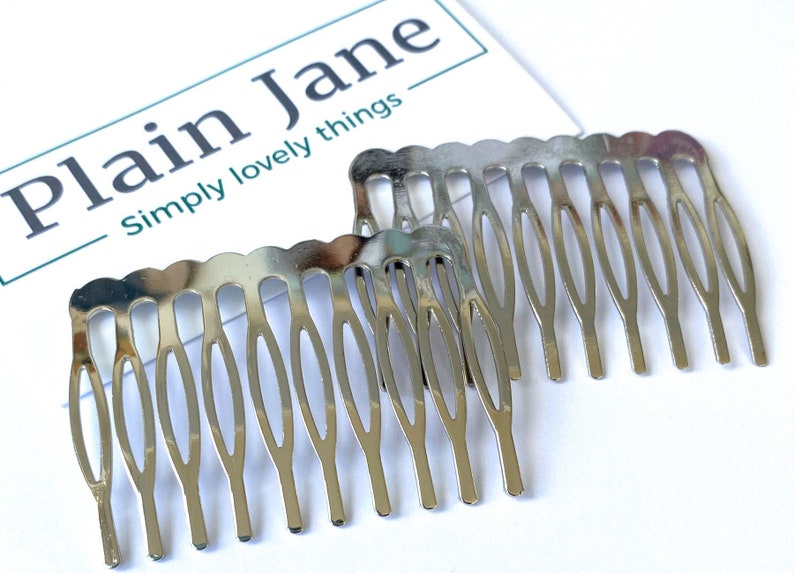 May include: Two silver hair combs with a decorative design. The combs are made of metal and have a shiny finish.