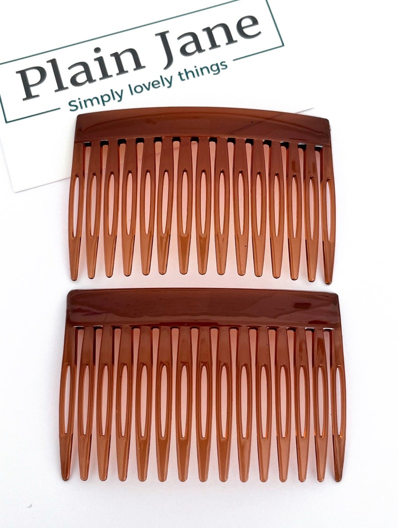 May include: Two brown plastic hair combs with a curved top and long teeth. The combs are side by side on a white background. The text "Plain Jane" and "Simply lovely things" is in the upper left corner.