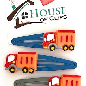 May include: Set of five red and orange toy truck hair clips. Each clip features a different design of a toy truck with three windows and black wheels. The clips are on a white background with a heart that says "Handmade" and a logo that says "House of Clips".