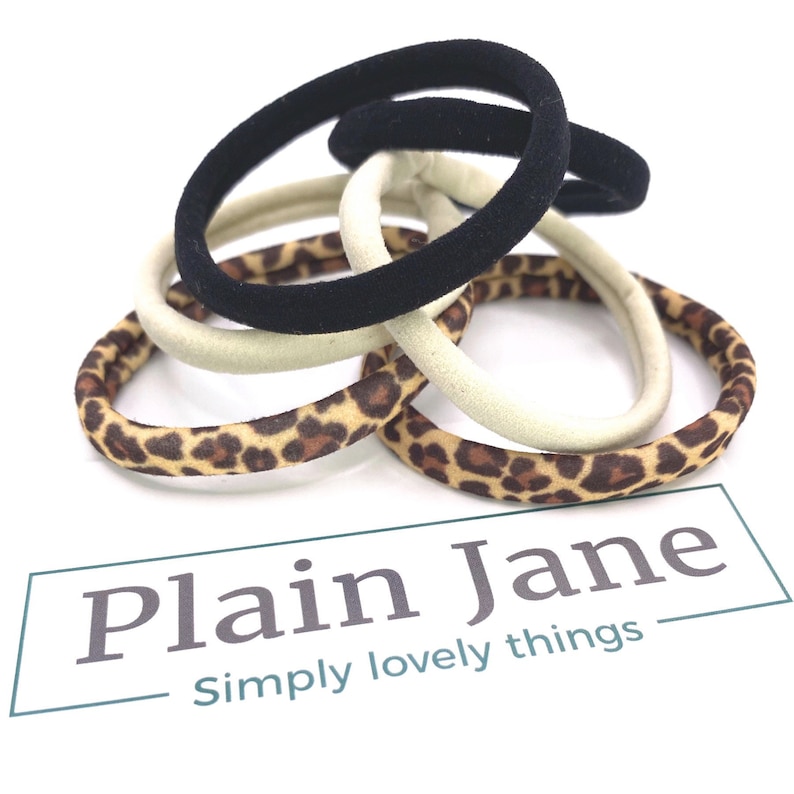 May include: A set of five hair scrunchies in a variety of patterns. Two are black, two are beige with a leopard print, and one is beige.